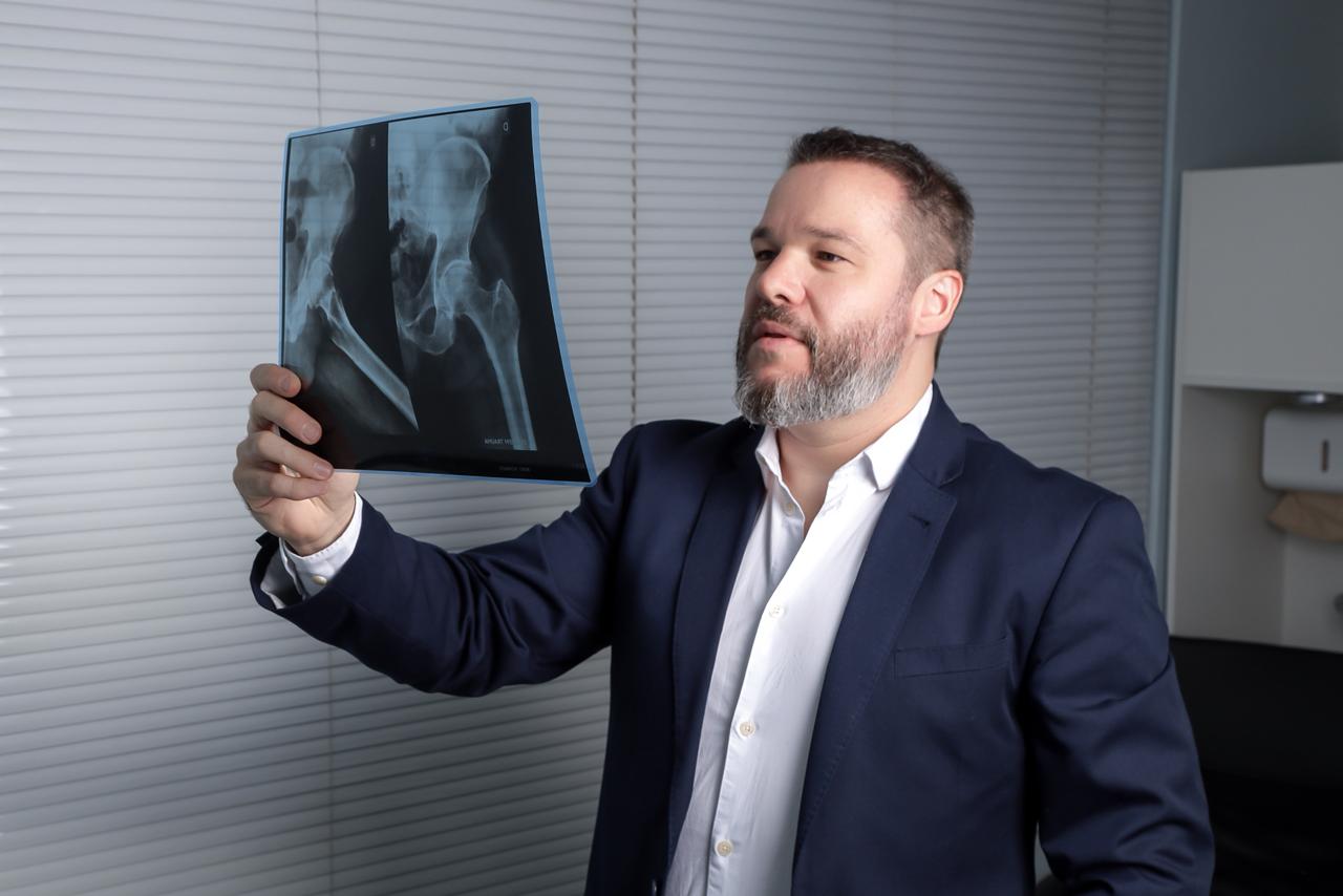 Dr. Ricardo analisando uma radiografia de quadril contra a luz da janela